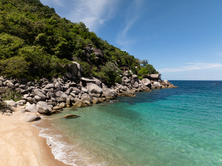 Tropical shoreline with rocky formations, lush greenery, and blue sea under sunny skies. Thailand, Koh Tao.の写真素材