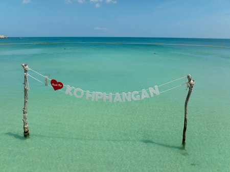 Koh Phangan sign above turquoise waters, supported by wooden poles, under a clear blue sky. Ko Pha Ngan, Thailand.の写真素材