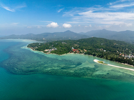 Coastal aerial view showcasing vibrant green landscapes and turquoise waters along the shoreline under a clear blue sky. Ko Pha Ngan, Thailand.の写真素材