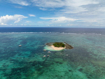 Top view of sandy island with palm trees surrounded by turquoise water and boats nearby. Guyam Island. Siargao, Philippines.の写真素材