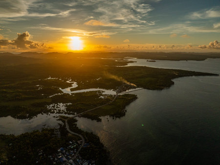 Sunset casts golden light over coastline, river estuary, and distant islands along the horizon....