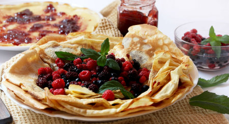 plate with fresh berries and pancakes filled with homemade jam placed over a napkin