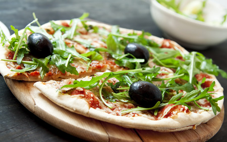 Pizza Margherita Closeup with Fresh Arugula Leaves and Olives on Wooden Boardの写真素材