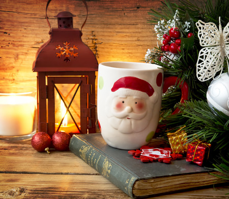 Santa's Cup on Warm Christmas Setting Background with Lantern, Old Book and Giftsの写真素材