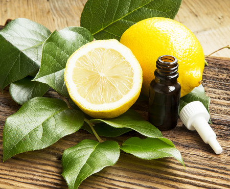 Lemon Essential Oil Bottle with Lemon Fruit and Leaves on Wooden Backgroundの写真素材