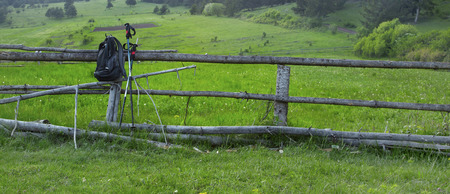 Countryside Landscape with Backpack and Trekking Poles Supported by Wooden Fence and Fresh Grassの写真素材