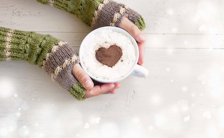 Holding Coffee Latte Cup with Cocoa Shape and Cozy Wool Hands Warmers on Magic Winter Backgroundの写真素材