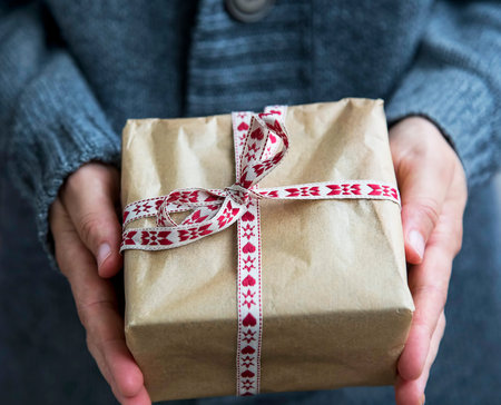 Female holding festive Christmas rustic gift decorated with ribbon