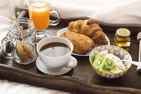 Breakfast in bed with coffee, granola and yogurt, orange juice and croissants in wooden trayの写真素材