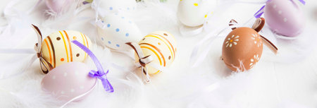 Easter eggs decorated with feathers on white painted wooden background