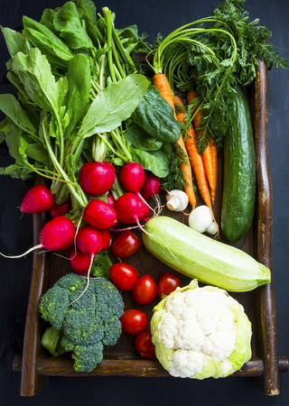 Fresh organic vegetables with carrots, cauliflower, broccoli, tomatoes, mushrooms, radishes on wooden trayの写真素材