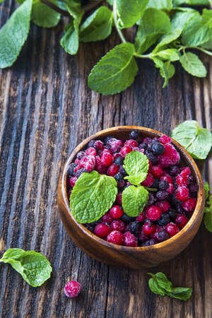 Fresh frozen fruits with currants, blueberries and mint leaves in wooden bowlの写真素材