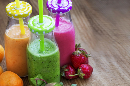 Fresh healthy three types of fruits juices or smoothies, orange, green and pink with strawberries, apricots,kiwi and spinach, smoothies bottle with strawsの写真素材