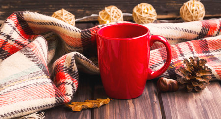 Cozy autumn blanket and tea cup , fall setting on wooden background with dried leaves and chestnutの写真素材