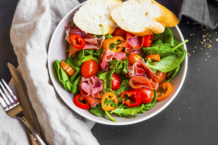 Fresh prosciutto ham salad with tomatoes , lettuce, spinach and pepper, fresh healthy vegetables salad with italian prosciutto in a bowl, top viewの写真素材