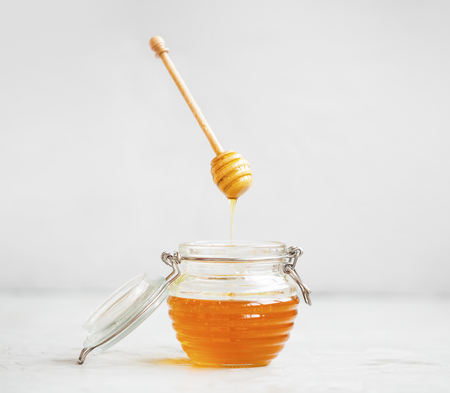 Raw organic honey jar with dipper that floats in the air with honey pouring in the glass jarの写真素材
