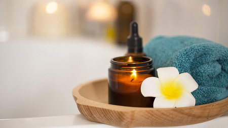 Spa setting with candle, frangipani flower, towel and body oil, bath home spa skin and body care treatmentの写真素材