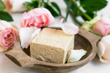 Spa still life with rose flowers and natural soap in wooden bowl closeup