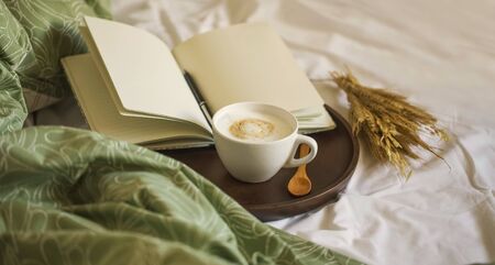 Cozy coffee cup cappuccino with notebook and pen in wooden board , morning bed coffee, vintage coffee cuo, morning coffee still lifeの写真素材
