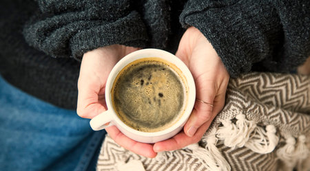 Interior cosy woman hands holding cup of coffee or chocolate with sweater and blanket, comfortable...