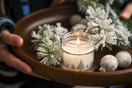 Winter cozy home deco rustic concept with woman holding wooden tray with fir tree branches and candle, cozy home conceptの写真素材