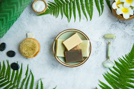 Spa still life flatlay with natural soap, green leaves, brush, face roller, frangipani flowers and...