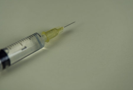 A syringe with liquid drop on coloured background