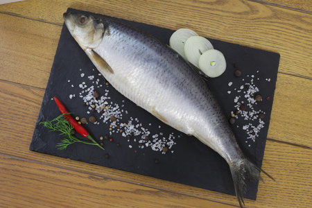 Sea salt herring undivided lies on a wooden board next to sliced onion rings and spicesの写真素材