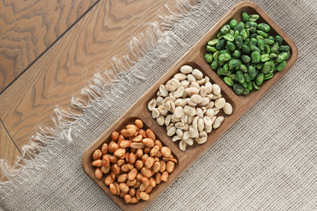 colorful roasted peanuts in a three-section wooden bowl that sits on a burlap tablecloth with no...