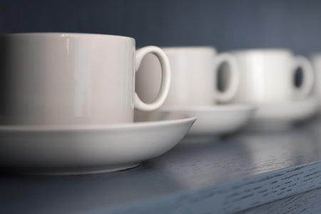 white porcelain teacups and saucers stand on a shelf with a wooden texture in blue-gray close-up without peopleの写真素材