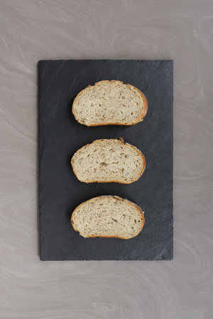 three pieces of grain bread lie on a black basalt board gray background close up view from above