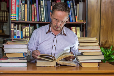 Senior business man sitting at his desk full of books  in the library