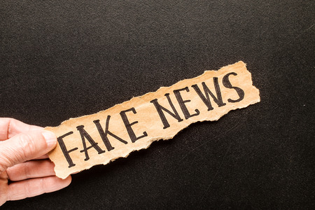 Torn paper with text FAKE NEWS   in his hand man, against the background of the chalk boardの写真素材