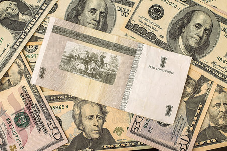 One Cuban pesos bill over several dollar bills