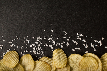 Crinkle cut potato chips on a blackboard. Tasty spicy potato chips with salt.Top viewの写真素材