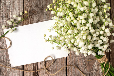 Bouquet of flowers lily of the valley and empty paper sheet on  rustic table from above, beautiful vintage card, top view, copy space for textの写真素材