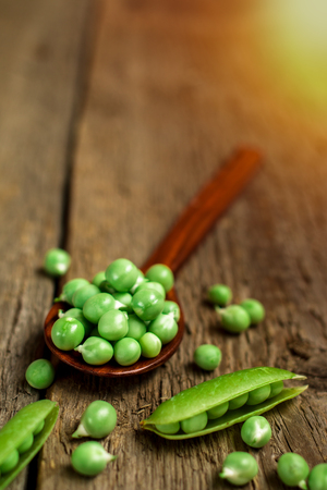 Green fresh peas in brown wooden spoonの写真素材