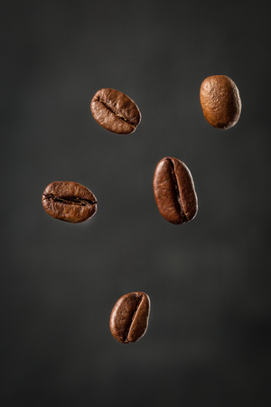 Grains of roasted coffee falling on gray background.  Levitation coffee beans. Food ingredients,  space for textの写真素材