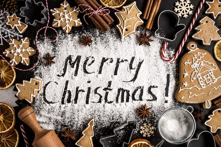 Inscription MERRY CHRISTMAS on powdered sugar  background  with fir-tree branches, orange fruits, gingerbread cookies and cones