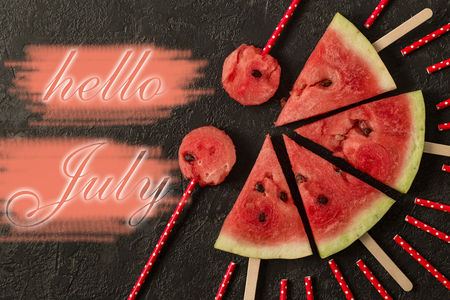 Watermelon slice with text Hello July. Summertime concept. on dark stone backgroundの写真素材