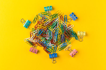 Colorful paper clips and binder clips on yellow background.