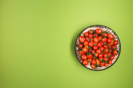 Flat lay with red tomatoes on green background, with copy space. tomatoes in a metal plate on bright...
