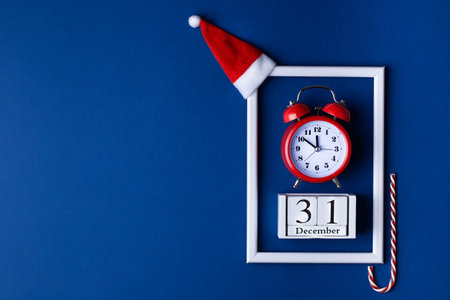 Christmas background composition. White photo frame with vintage alarm clock on a blue classic...