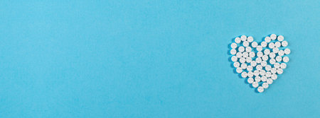 Heart shape made of pills on blue background.