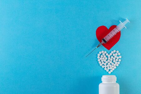 Heart shape made of pills and syringe on blue background.の写真素材