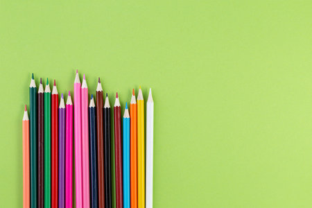 Colored pencils on a green background. Colorful wooden pencils. Flat lay, Top view with copy space