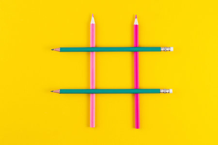 Hashtag sign from crossed colorful pencils on yellow background.
