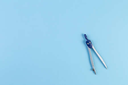 School compass for drawing circles in geometry. Isolated on blue paper background. back to school concept with stationery. With copy space, template for text or designの写真素材