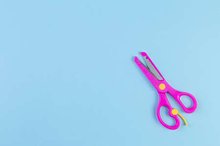 Minimalist photo of pink children's scissors on blue background. back to school concept with stationery. With copy space, template for text or design. Top view, Flat layの写真素材