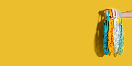 Male hand holding empty netted bags on yellow background. Eco friendly zero waste bag.